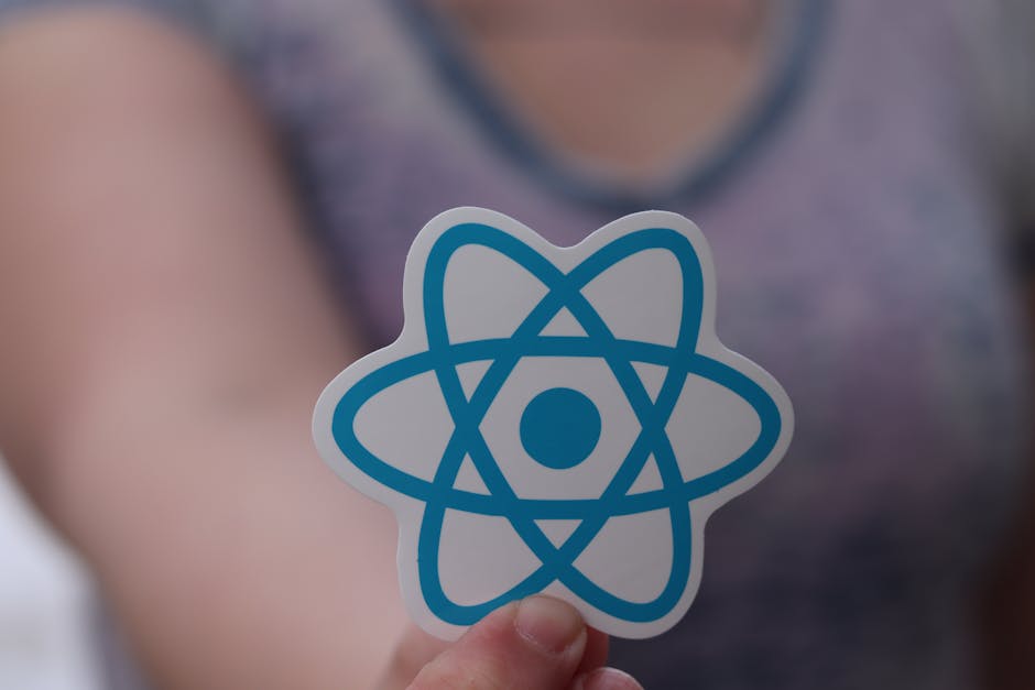 A close-up of a person holding a small, flat, white sticker with a blue atomic model symbol on it, with the person wearing a grey patterned top. The background is blurred, focusing on the atom symbol 